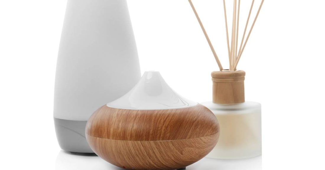 A close-up of three types of aroma oil diffusers on a white background. Two are electric, and one is a reed diffuser.